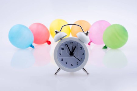 Foto de Reloj despertador y pequeños globos de colores sobre un fondo blanco - Imagen libre de derechos