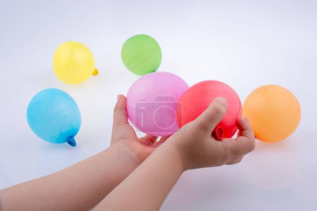 Téléchargez les photos : Main tenant un petit ballon coloré avec des ballons colorés sur le fond blanc - en image libre de droit