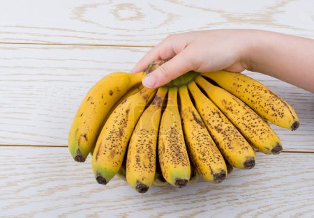 Foto de Mano sosteniendo racimo de plátanos pecosos en una textura de madera - Imagen libre de derechos