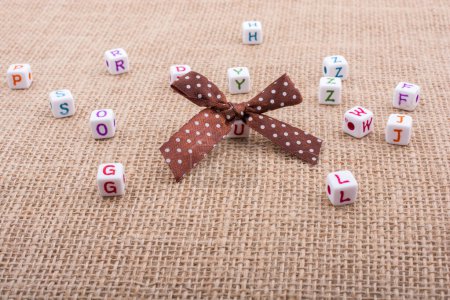 Photo for A ribbon and scattered dice-sized alphabet cubes on a textured surface in display - Royalty Free Image