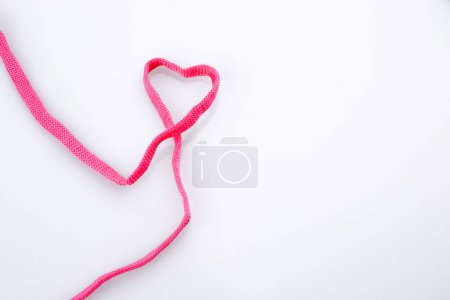 Corazón hecho con la ayuda de un sholace rosa sobre fondo blanco
