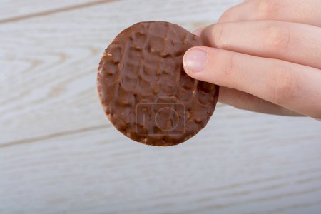 Téléchargez les photos : Main tenant un biscuit recouvert de chocolat sur un fond en bois - en image libre de droit