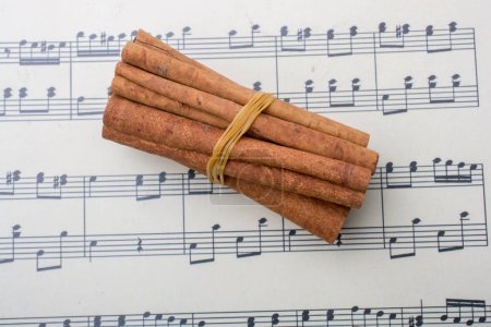 Téléchargez les photos : Des paquets de bâtonnets de cannelle placés sur un papier avec des notes de musique - en image libre de droit
