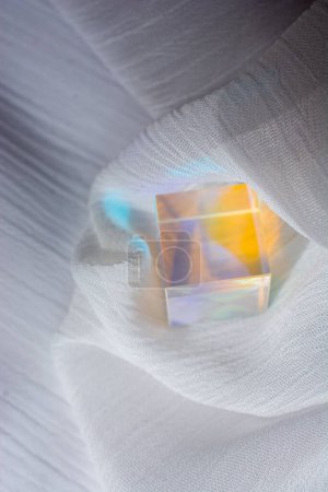 Glaswürfel mit Farbspektrum-Strahlen auf Stoff. Abstrakter Hintergrund mit Reflexion und Lichtbrechung.