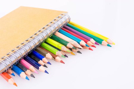 Foto de Lápices de varios colores cerca de un cuaderno sobre un fondo blanco - Imagen libre de derechos