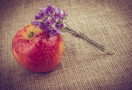 Winziger Blumenstrauß neben einem Apfel auf Leinwand