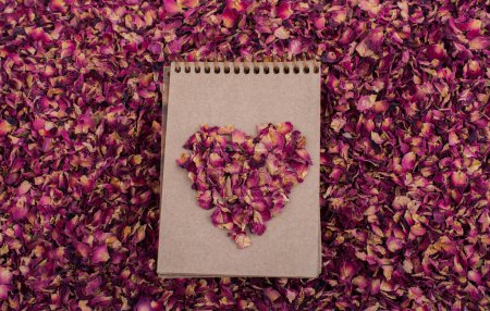 Foto de Pétalos de rosa seca forman una forma de corazón en un cuaderno en espiral - Imagen libre de derechos