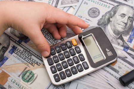Téléchargez les photos : Le tout-petit tient une calculatrice sur le billet de dollars américains étalé autour de - en image libre de droit