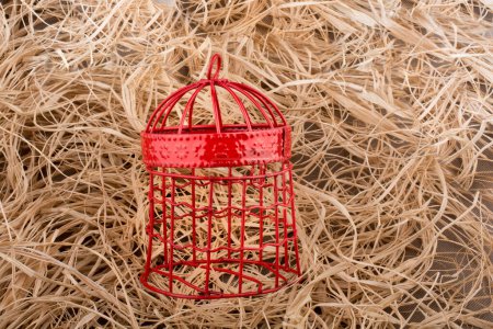 Téléchargez les photos : Cage à oiseaux de couleur rouge placée sur un fond de paille - en image libre de droit