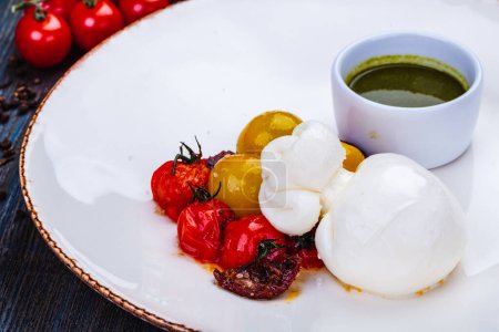 Photo for Burrata cheese with baked cherry tomatoes and pesto sauce on white plate. - Royalty Free Image