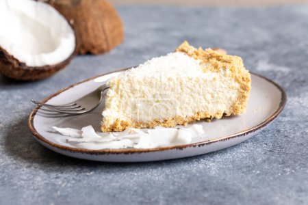 piece of coconut cheesecake on a plate with fresh coconut.