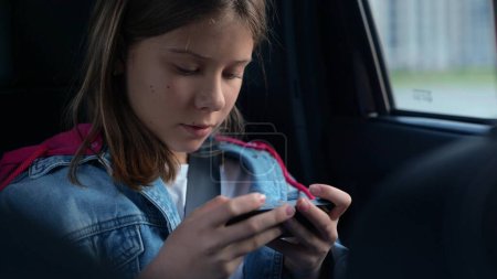 Photo for Close up of pretty teenage girl sitting in car and using smartphone playing video game online. Kid teen surfing the internet on mobile phone on family trip in automobile. Technology, leisure concept - Royalty Free Image