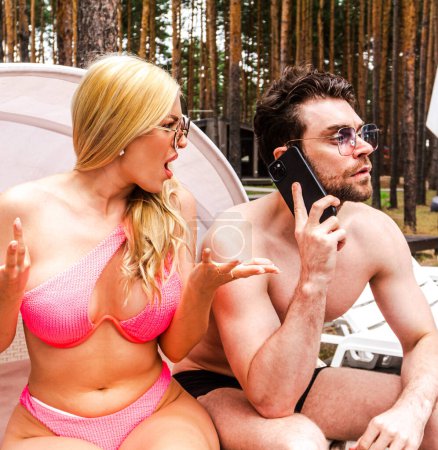 Young man talking on the mobile phone while woman woman outraged. Couple sitting on the sunbed. Summer vacation, relationship, lifestyle concept
