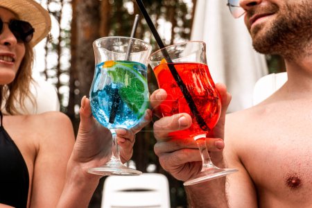Moderna pareja joven en gafas de sol de moda tintineo vasos con bebidas refrescantes mientras se miran al aire libre. Actividad de ocio y concepto de vacaciones de verano