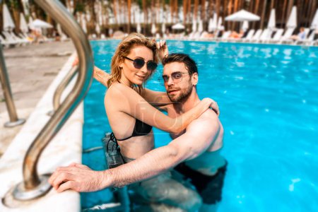 Mujer atractiva y agradable en bikini apoyada en los hombros de su lindo novio en la piscina. Concepto de Romance y vacaciones de verano