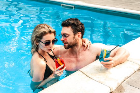 Verliebter Mann umarmt seine schöne Freundin und schlürft in seinem Beisein in einem Freibad einen Cocktail. Romantik und Sommerferienkonzept