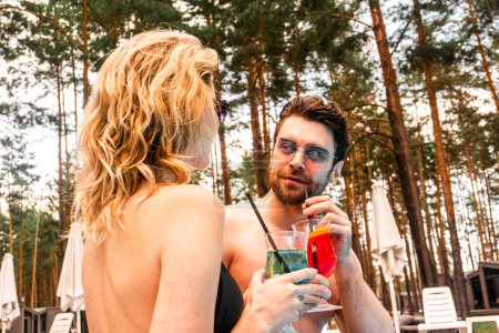 Photo for Handsome dark-haired young man in sunglasses and a blonde woman drinking refreshing beverages while sitting together outdoors. Rest and relaxation concept - Royalty Free Image