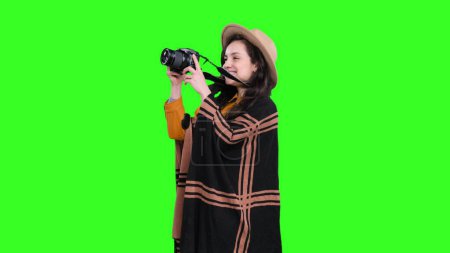 Lächelnde hübsche Frau mit Hut auf Reisen, während sie Fotos mit der Kamera auf grünem, isoliertem Hintergrund macht. Reise, Tourismus, Abenteuerkonzept