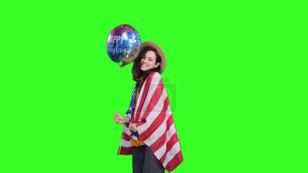 Mujer joven con bandera de EE.UU. sobre sus hombros sosteniendo colorido globo sobre fondo verde aislado. Fiesta, celebración, concepto patriótico