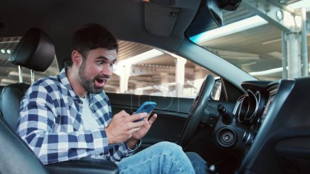 Erfolgreicher junger Mann, der im Auto auf den Smartphone-Bildschirm schaut und Nachrichten liest. Transport, Technologie, Lifestylekonzept. Zeitlupe