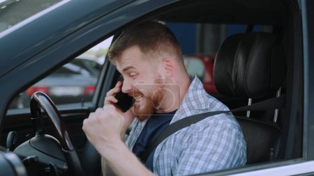 Successful young man wearing seat belt in the car, talking on the phone. Transport, technology, trip concept. Slow motion
