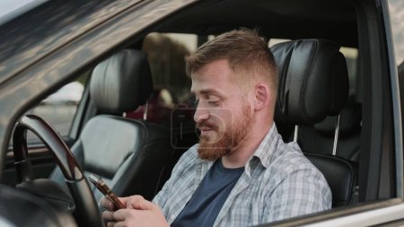 Lächelnder junger Mann am Fahrersitz, während er auf dem Handy tippt. Transport, Technik, Reisekonzept. Zeitlupe