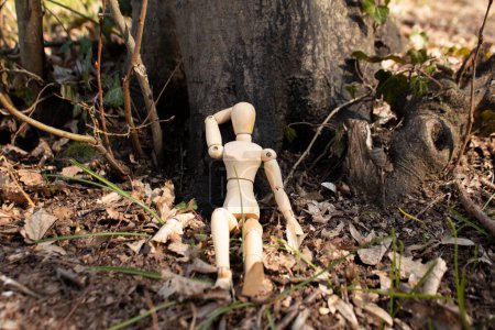 Téléchargez les photos : Mannequin en bois assis devant le corps de l'arbre, marionnette en bois faire une sieste sur la forêt, vue de face, détente et refroidissement, concept d'automne - en image libre de droit