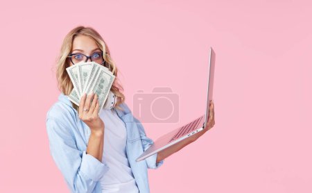 Porträt eines fröhlichen Teenie-Mädchens in lässiger, denimblauer Kleidung mit einem Laptop in der Hand auf rosa Hintergrund. Das Konzept des Lernens und der Online-Jobsuche