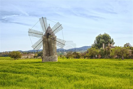 Ancient windmill on green meadow with blue sky and hill at background, Mallorca. Famous tourist attractions in Mallorca - over 5000 windmills all over the island
