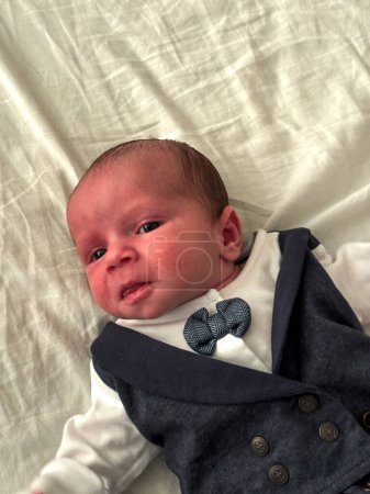 Un hermoso retrato de bebé de un recién nacido. El niño está vestido con elegancia, con un traje de tres piezas, corbata de lazo y gorra plana.