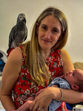 Une première mère tenant son fils nouveau-né, son perroquet gris africain est perché sur son épaule