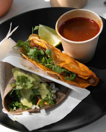 Foto de Tacos barbacoa, con su consomé en el lado, tacos mexicanos en placa de cerámica negra. mexico latinoamerica - Imagen libre de derechos