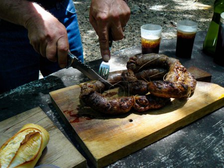 Hombre inidentificable cortando una tradicional barbacoa argentina con un cuchillo