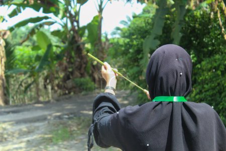 Simalungun Indonesia, january 14, 2024- a woman aims at something with a traditional toy weapon made from bamboo or called a pletokan.  portrait of woman from behind