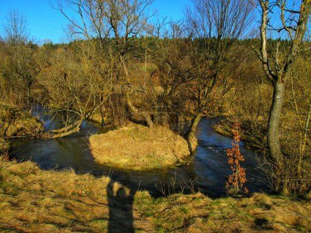 Peaceful river curving through a spring landscape with photographer's shadow