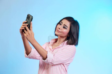 Photo for Image of beautiful Hispanic girl taking her selfie  on phone isolated over gradient blue background - Royalty Free Image