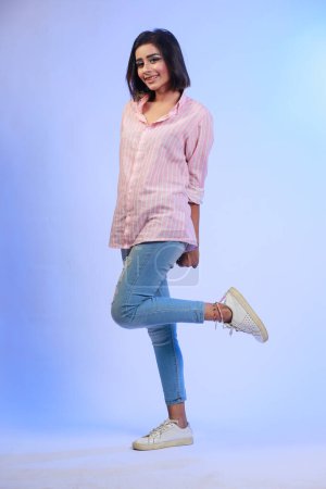 Foto de Young attractive Pakistani Indian Girl, in Jeans and a button down shirt, Posing and giving feeling cute expressions on a blue gradient studio background - Imagen libre de derechos