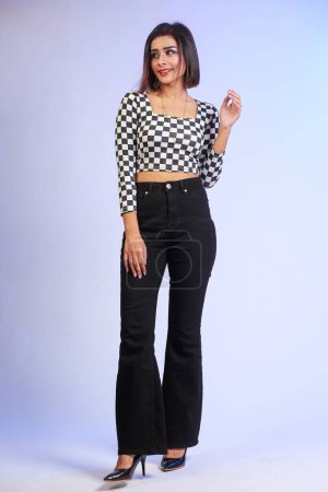 Photo for Young stylish bold fit and slim girl walking casually, looking in camera isolated on a studio background. The girl is wearing black and white trendy shirt with black bell bottom pants and high heels - Royalty Free Image