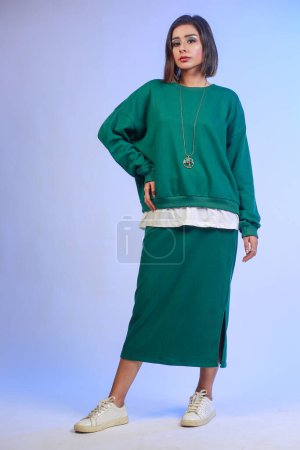 Photo for Magnificent high fashion woman in long green skirt Posing in studio. Carefree inspired female model posing with pleasure on gradient blue background. - Royalty Free Image
