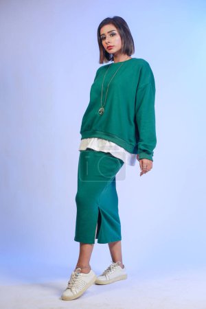 Téléchargez les photos : Magnifique femme en jupe longue verte dansant en studio. Modèle féminin inspiré sans soucis posant avec plaisir sur fond bleu dégradé. - en image libre de droit