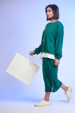 Photo for Hipster girl with short hair wearing green sweatshirt and a skirt, walking with a white paper bag, Shopping concept - Royalty Free Image
