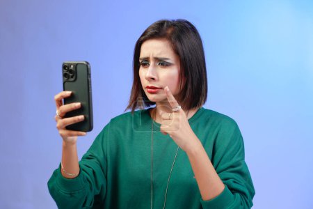 Photo for Angry hipster girl point aside jealous, something unfair, complaining and looking disappointed, sulking and frowning, standing displeased while on a video call wearing a trendy green sweatshirt - Royalty Free Image