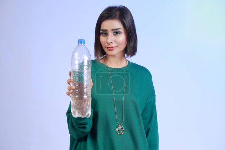 Téléchargez les photos : Young Pakistani girl holding plastic water bottle. Hydrate and stay healthy. Presenting a transparent plastic unbranded water bottle. Selective Focus. - en image libre de droit