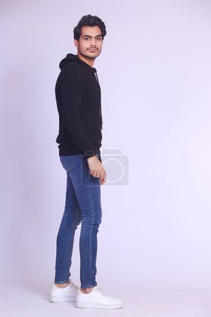 Foto de Side view of handsome confident cool young guy with hoodie looking right in camera. Full body length portrait isolated over white studio background. - Imagen libre de derechos