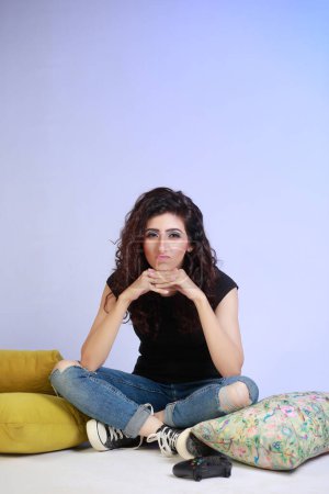 Photo for Cheerful girl with curly hair , sitting on the floor with cushions around and feeling bored - Royalty Free Image
