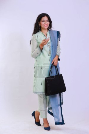 Téléchargez les photos : Pakistani woman in traditional kameez shalwar dress, talking on a phone call, carrying a hand bag - en image libre de droit