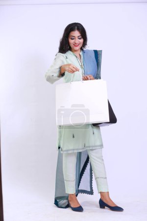 Foto de Joven mujer paquistaní de moda caminando después de ir de compras con una bolsa de papel mirando en la cámara. La imagen retrata a la chica está feliz con su compra. Aislado sobre fondo blanco - Imagen libre de derechos