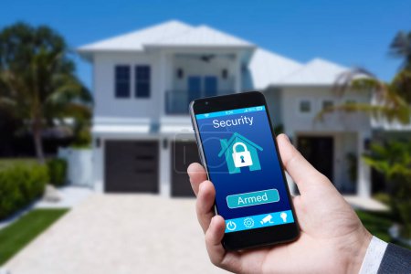 Photo for Smartphone with home security app in a hand on the building background - Royalty Free Image