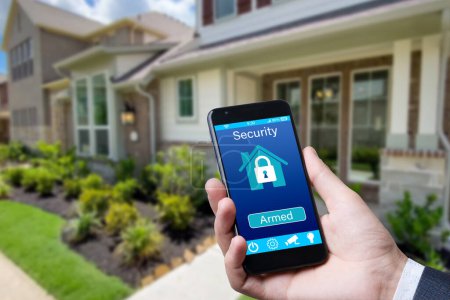 Téléchargez les photos : Smartphone avec application de sécurité à domicile dans une main sur le fond du bâtiment - en image libre de droit