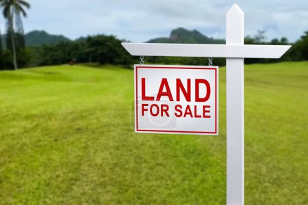Land for sale sign in green grass field for housing development and construction background
